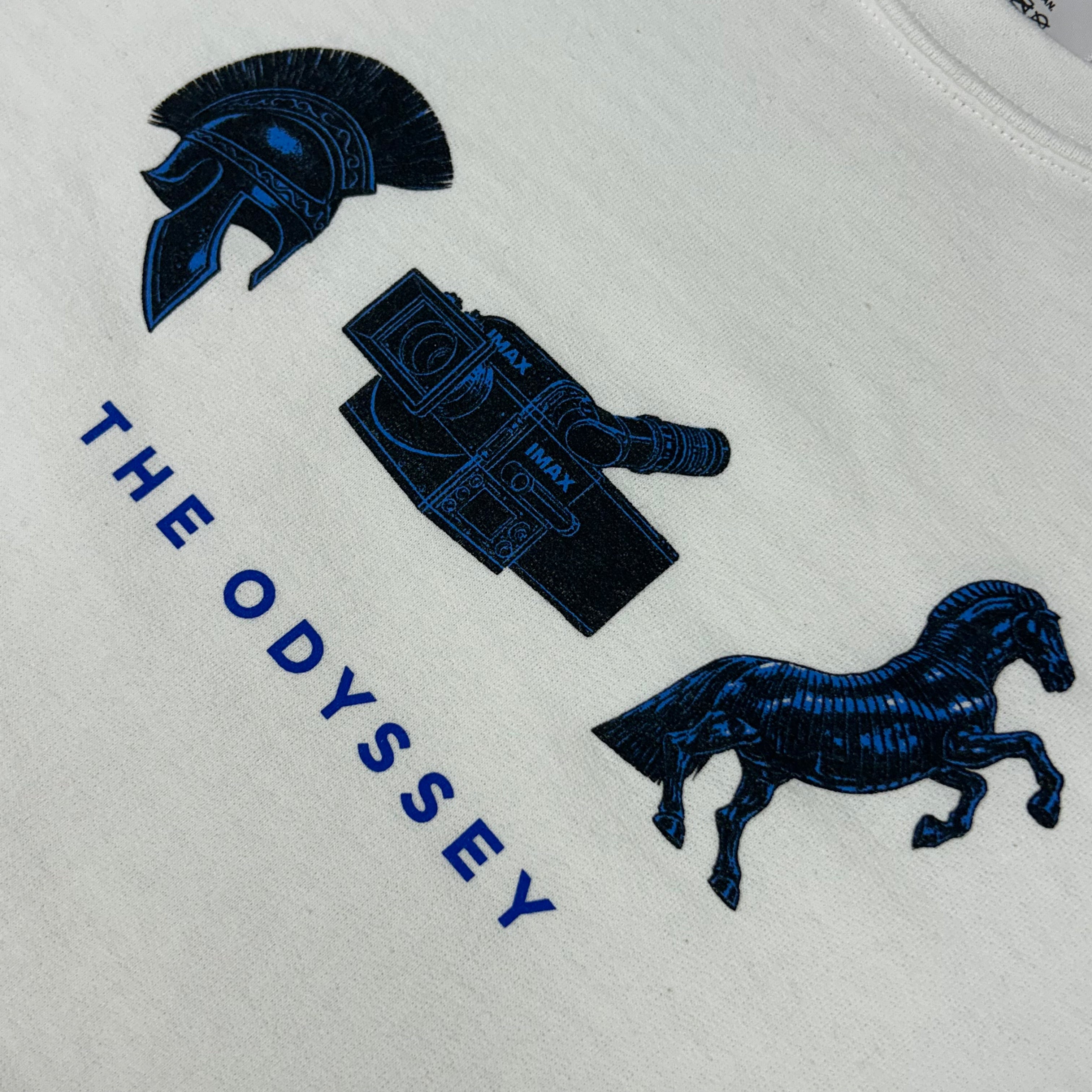 Embroidered design on a white fabric with blue patterns including a helmet, shield, and horse, with 'The Odyssey' text.