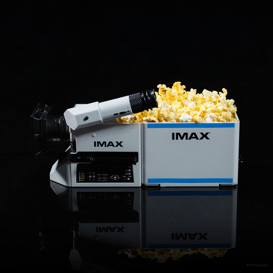 Collectible popcorn container designed to resemble an IMAX Film Camera, featuring a white body with black and blue IMAX and The Odyssey branding, a viewfinder, and camera lens detail, shown on a white background.
