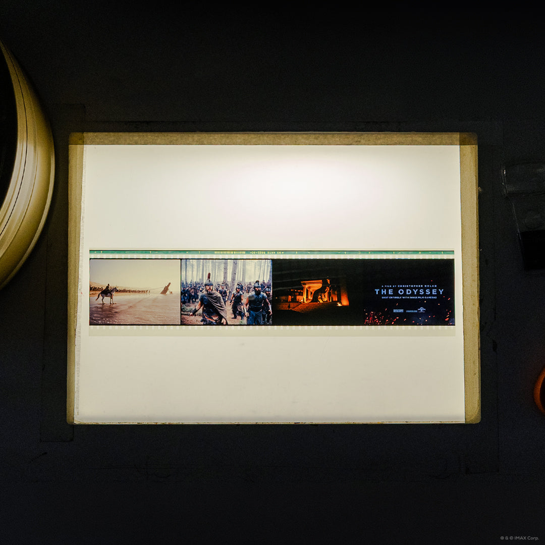 An IMAX 70mm filmstrip featuring 3 scenes from the movie The Odyssey: a shoreline with the Trojan horse in the back, warriors in battle, a firelit temple, and the film title card.