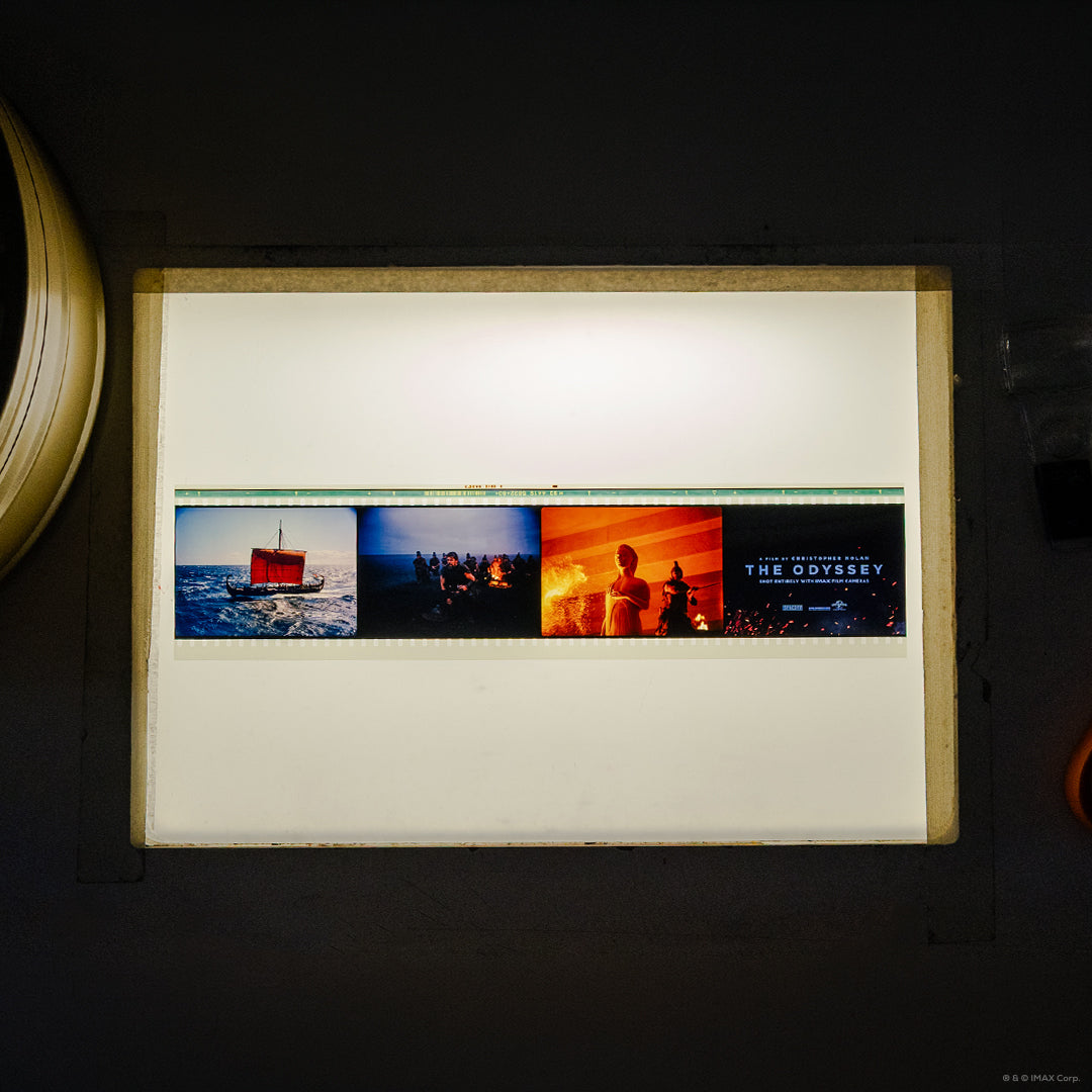 An IMAX 70mm filmstrip featuring 3 scenes from the movie The Odyssey: a red-sailed ship at sea, a group gathered around a fire, figures in warm orange light, and the film title card.