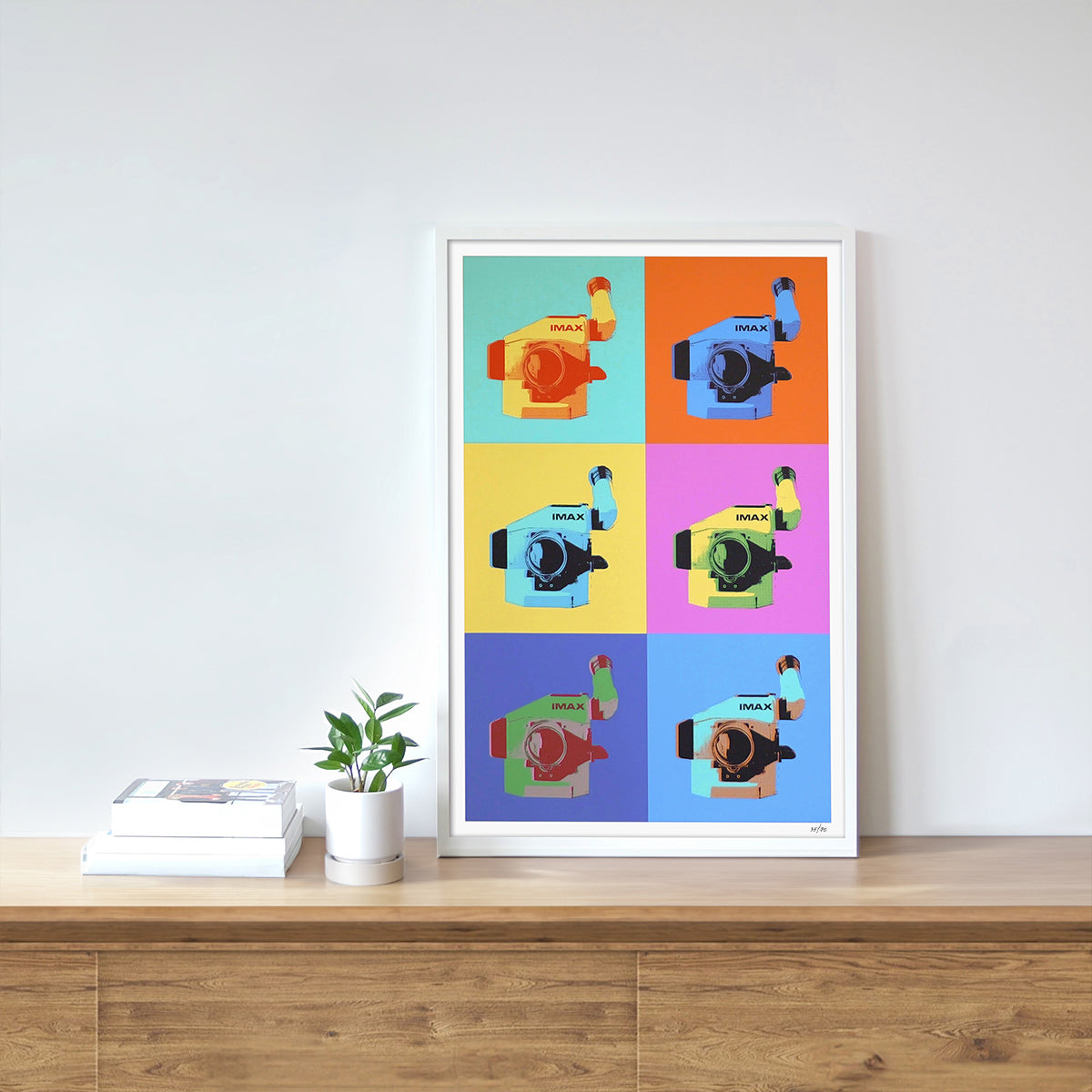 A framed multicolored poster on a shelf, featuring several IMAX film cameras arranged in various colored boxes.