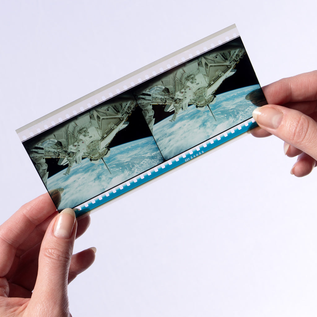 A pair of hands holding an IMAX filmstrip featuring outer space imagery from the IMAX documentary The Dream is Alive.