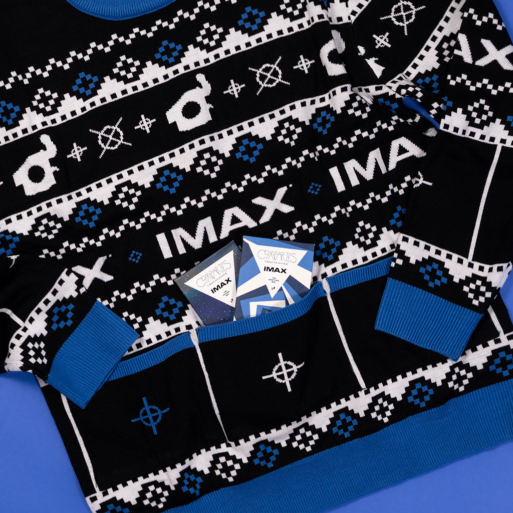 A festive black and blue holiday sweater featuring various camera-related logos, IMAX logo, with 3 pockets on the front and candy tucked in the pockets.