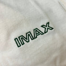 Close-up of 'IMAX' logo embroidered on a light cream fabric background
