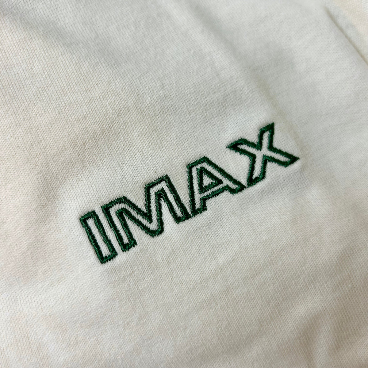 Close-up of 'IMAX' logo embroidered on a light cream fabric background