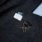 A close-up on a silver clapper board and black director’s chair enamel pins placed on a dark grey crewneck sweatshirt.
