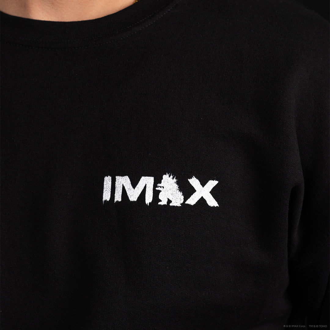Close-up of a black crewneck sweatshirt featuring a white distressed 'IMAX' logo across the chest, worn by a model.