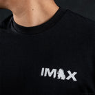 Close-up of a person wearing a black crew-neck t-shirt with a white distressed 'IMAX' logo printed on the chest.