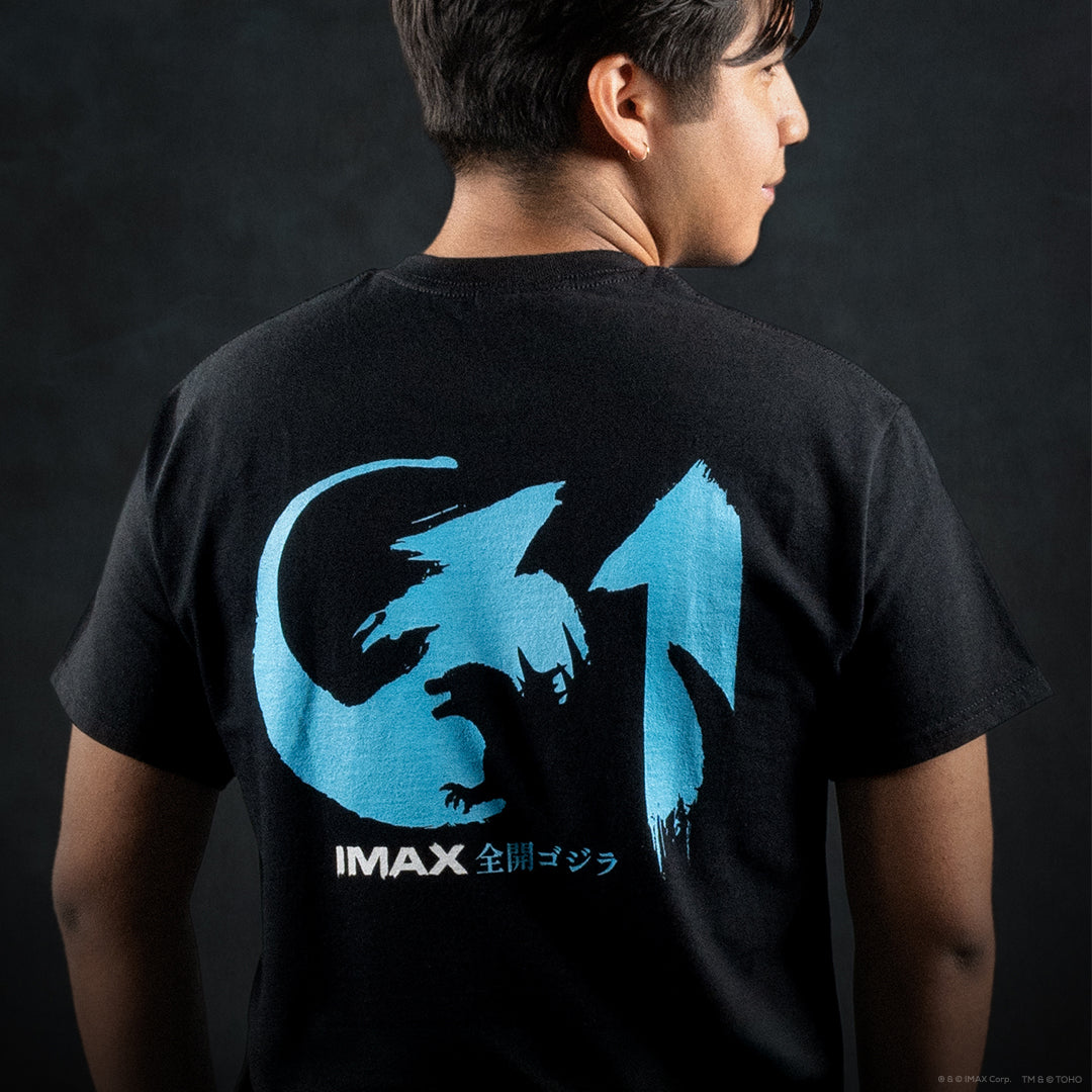 A person shown from the back wearing a black t-shirt with a large blue Godzilla graphic and white IMAX text on the back, set against a dark textured background.