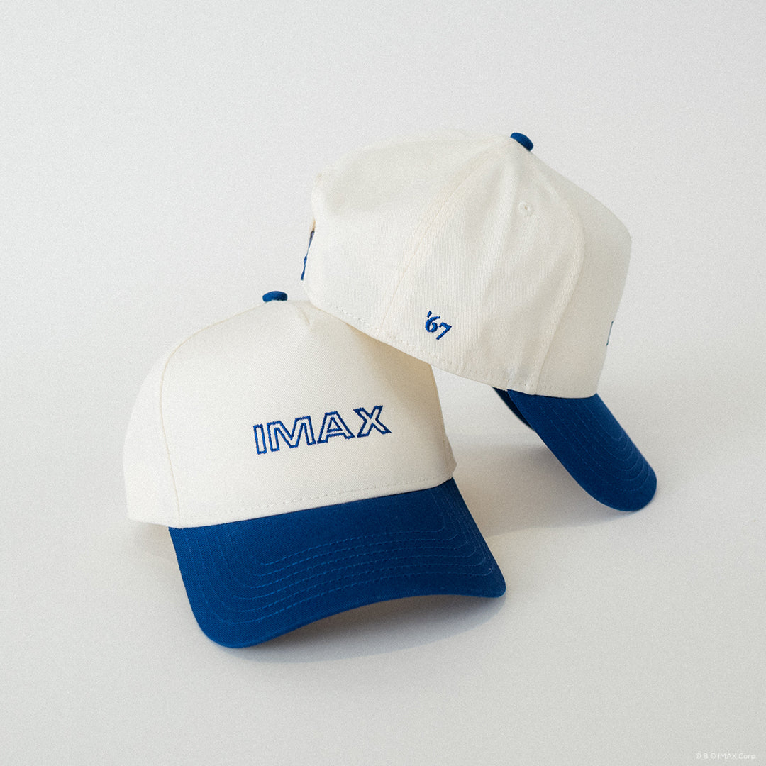 Two white and blue caps with 'IMAX' and '67' text on a light gray background