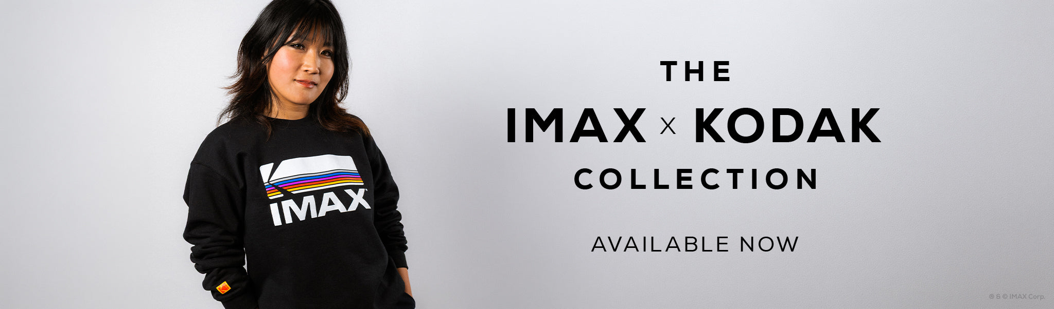 Person wearing a black crewneck sweatshirt that has a Kodak logo and IMAX text under it. Text that reads "THE IMAX x KODAK COLLECTION AVAILABLE NOW"