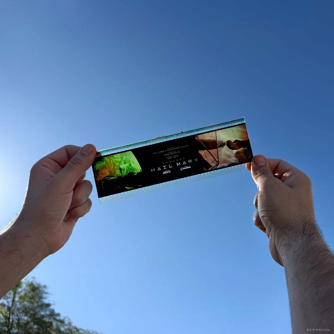 Image of an IMAX 70mm filmstrip featuring scenes from Project Hail Mary, with a green-toned space landscape on the left, a warm orange-lit close-up on the right, and the film title centered with “Filmed for IMAX” branding