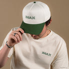 Person wearing Cream and green cotton baseball style hat hat featuring embroidered IMAX outline logo on the front, curved green brim, and adjustable back strap and embroidered “’67” detail on the side.