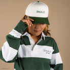 Person wearing a Green and white striped rugby style long sleeve polo with a white collar. Green embroidered IMAX est 1967 small on the left chest. They are also wearing a matching green and cream hat with IMAX logo on the front. 
